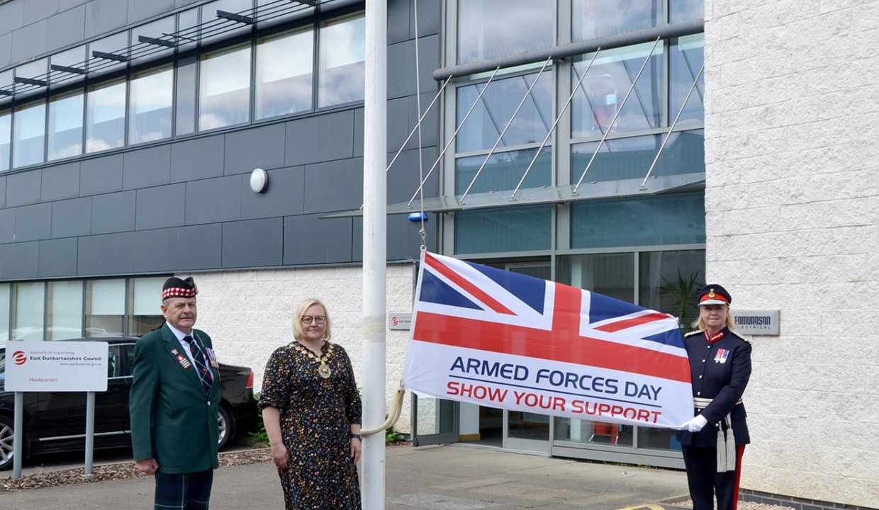 Provost with current and retired military staff holding the armed forces day flag
