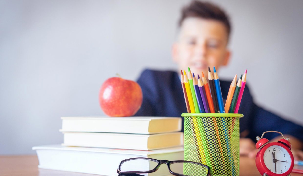 Boy sitting at desk with books and pens on it.